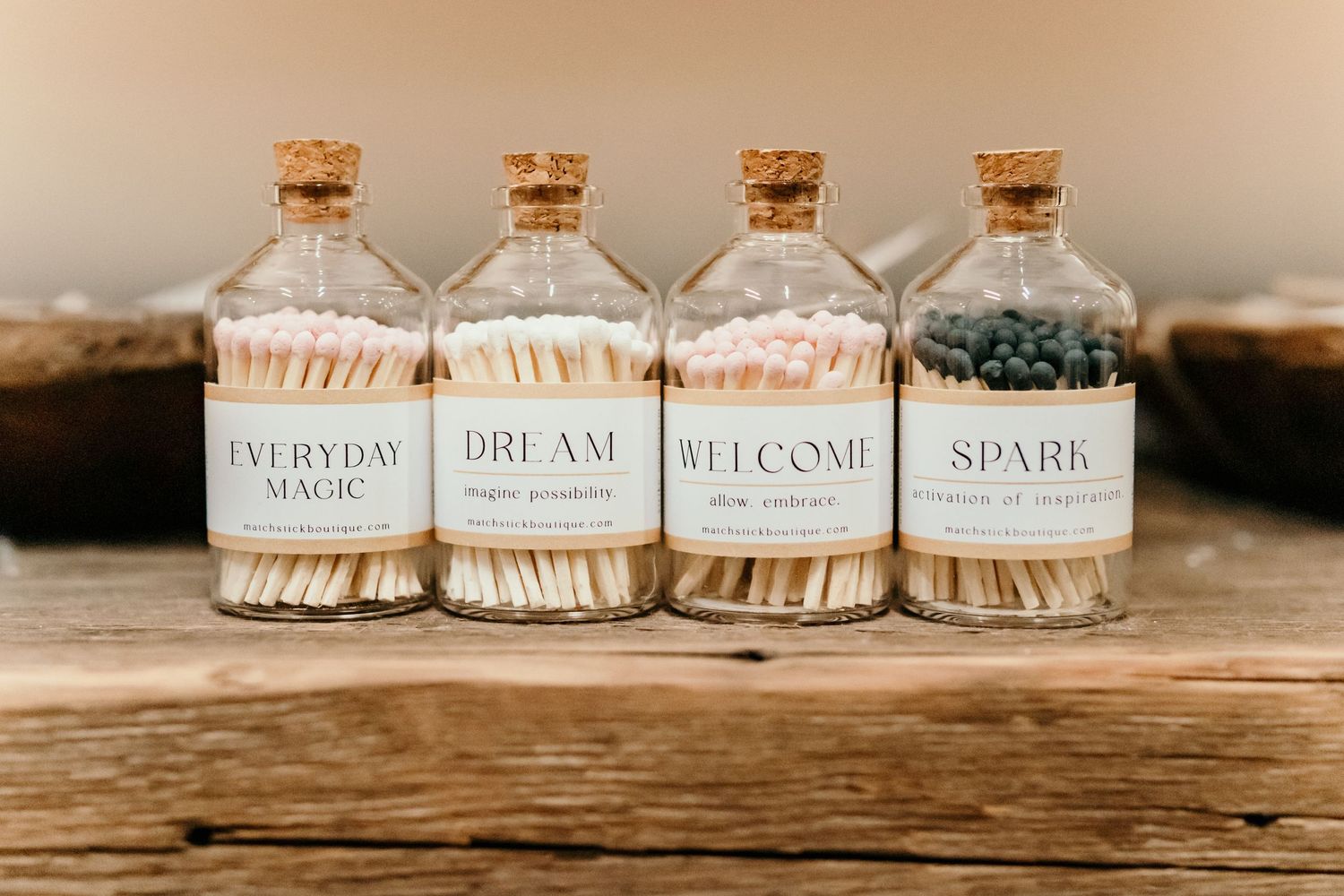 Small glass jars with cork lids displaying inspirational words like 'everyday', 'dream', 'welcome' and 'spark' on wooden surface.