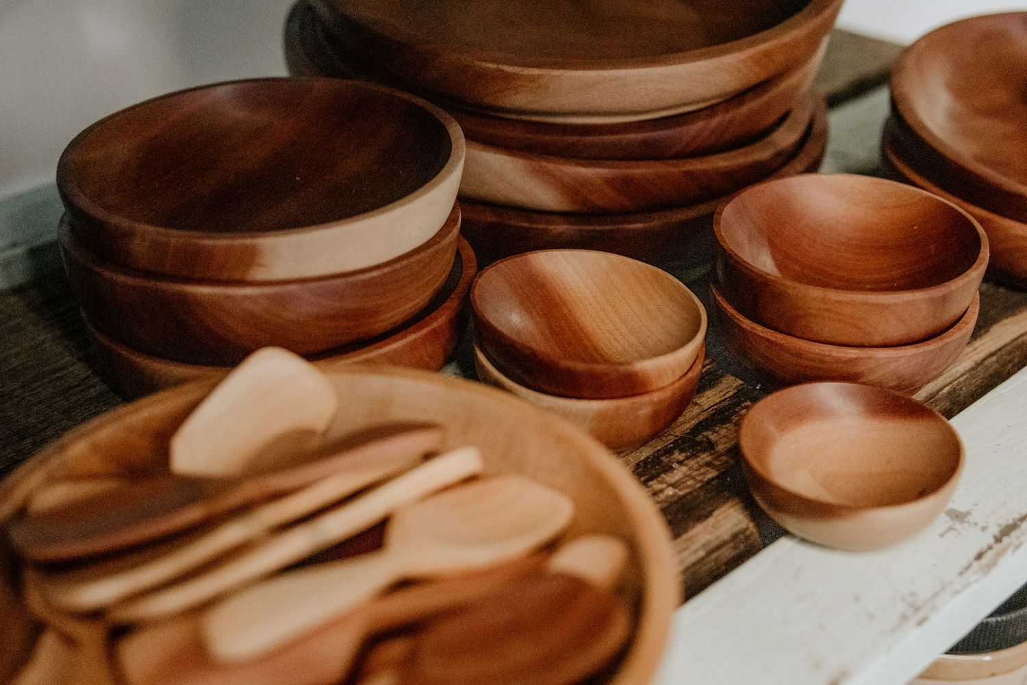 Artisanal wooden bowls and spoons displayed in warm lighting on wooden background.