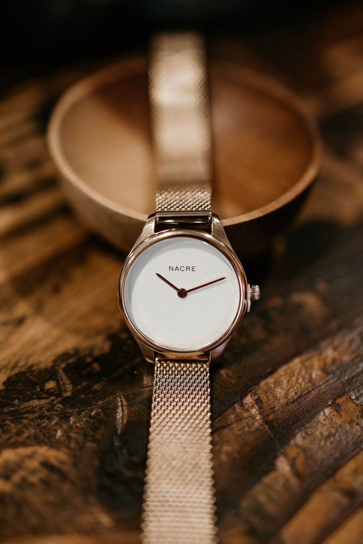 Elegant silver mesh band watch with clean white dial displayed on textured wood.