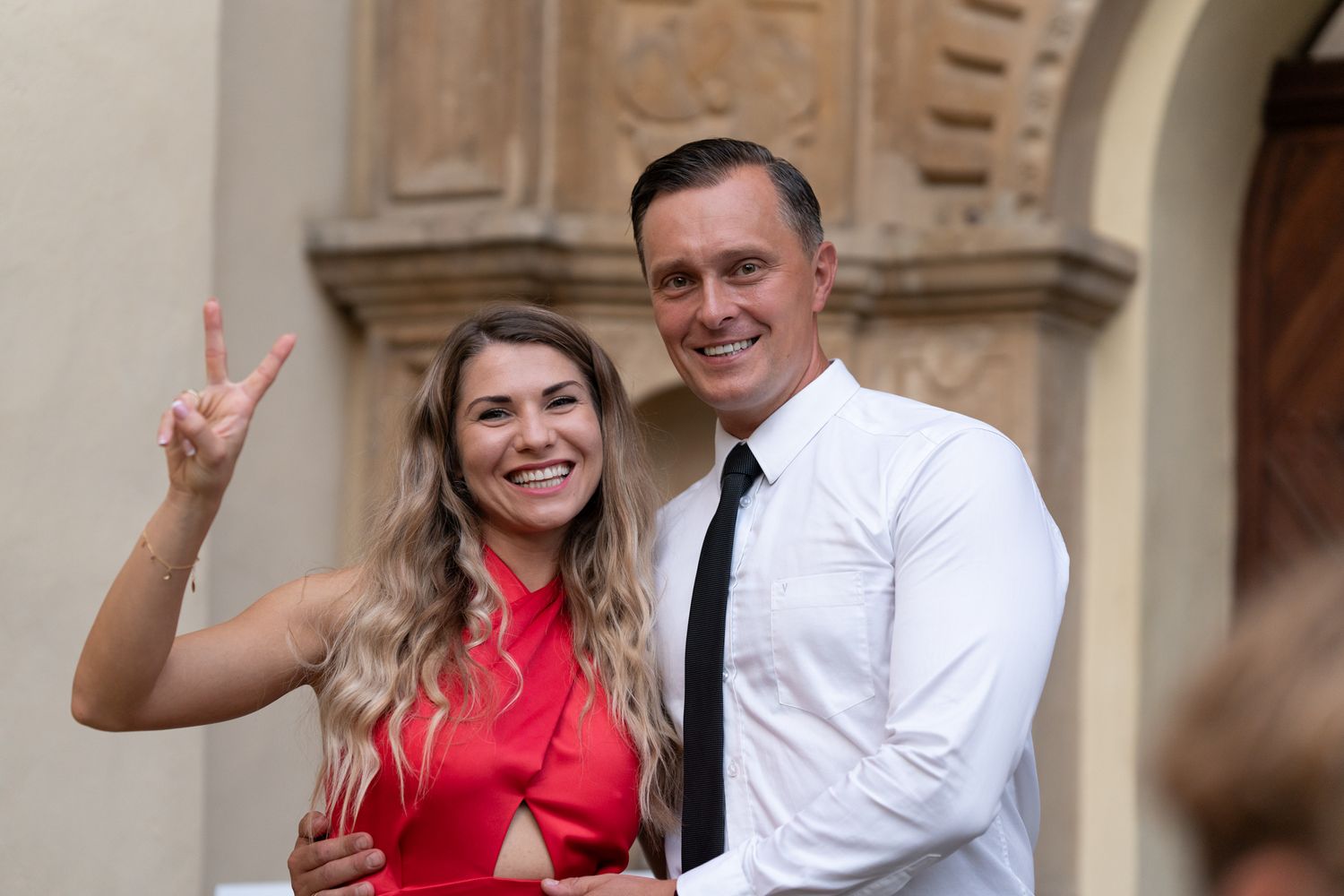 Cheerful couple in formal attire sharing candid moment outside historic building.
