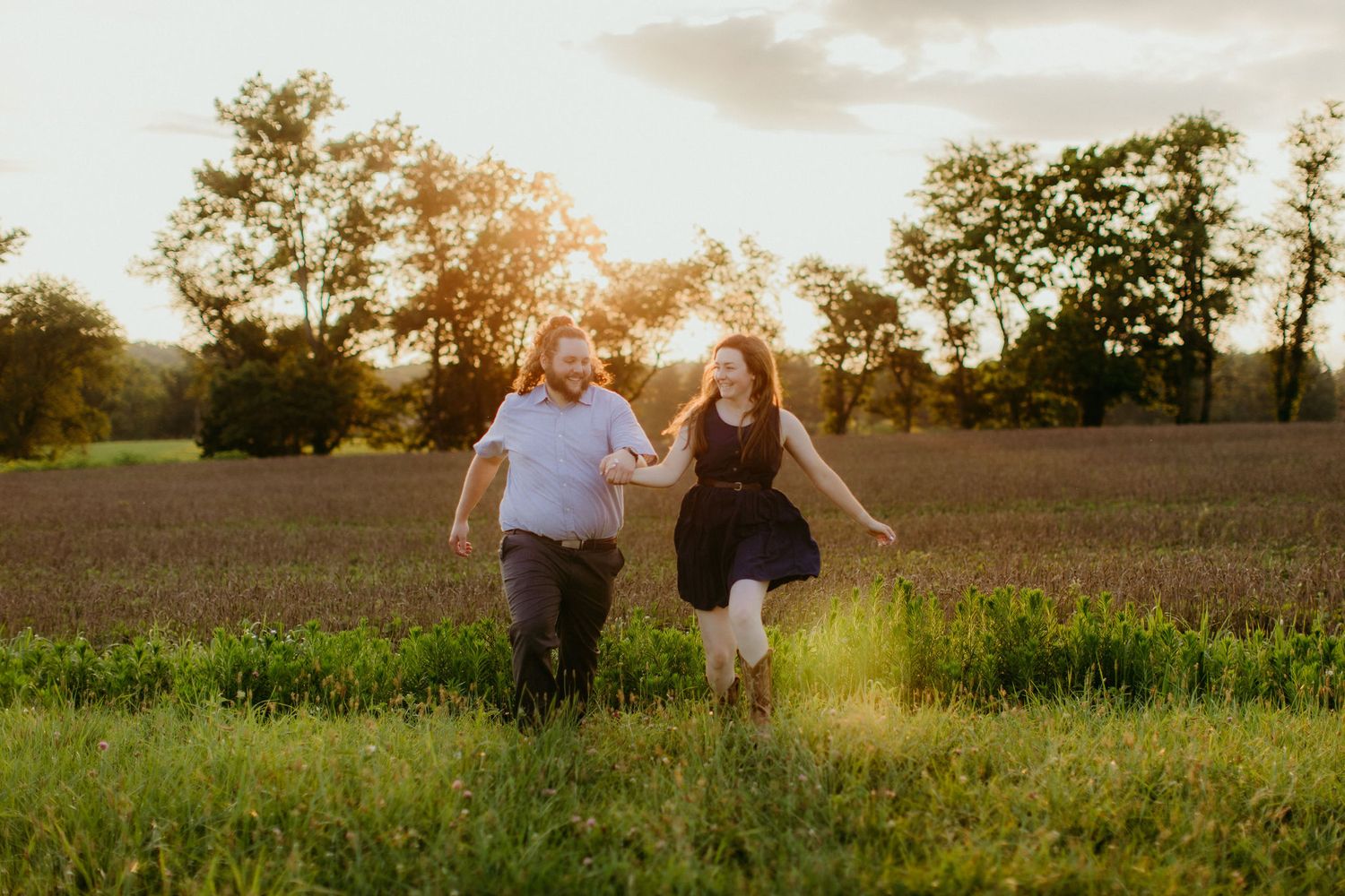 the couple runs together through a field at sunset. the sun is at their back causing a golden glow to surround them.