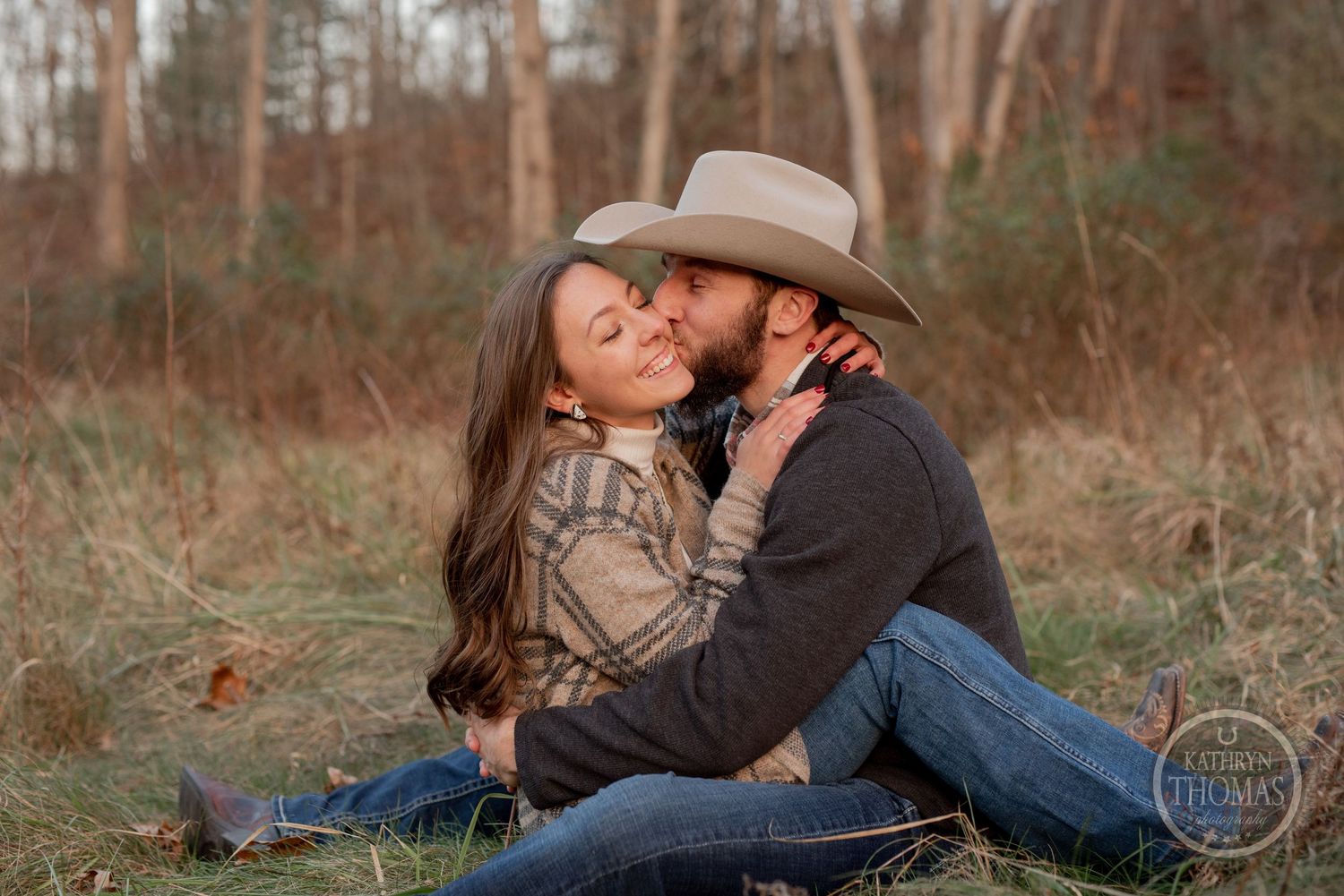 A romantic moment between a couple sitting in tall grass during golden hour.