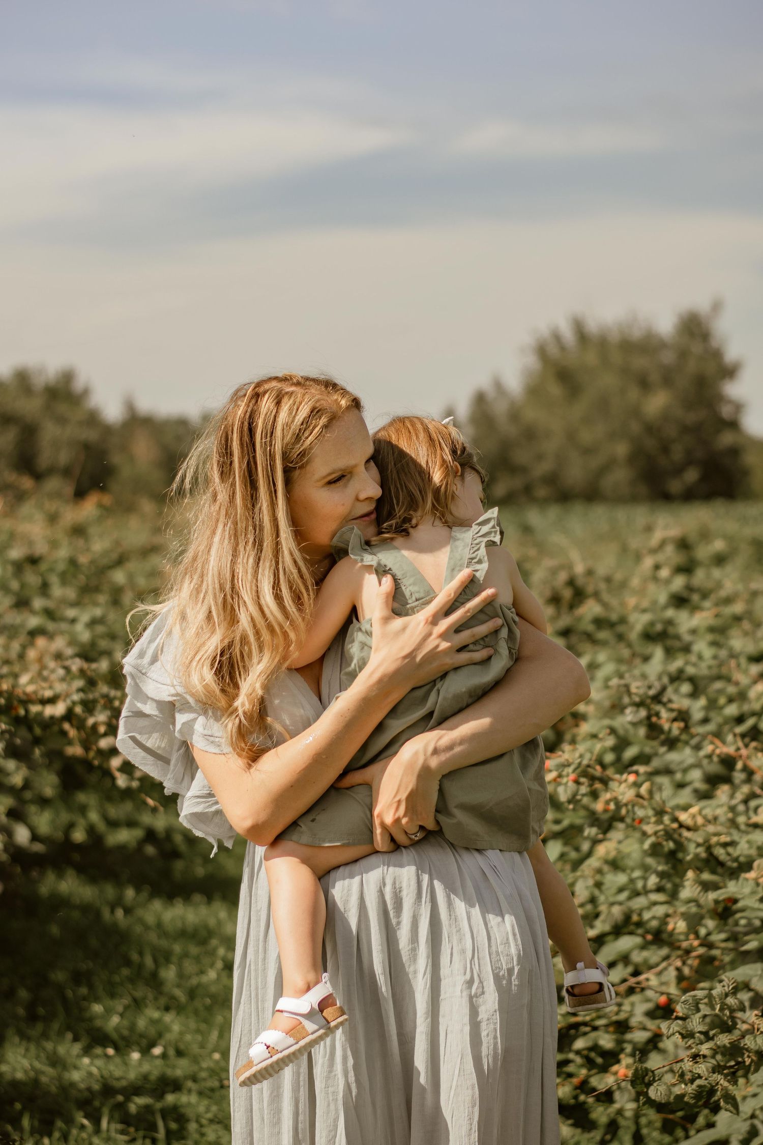 A tender moment between parent and child in a sunny field wearing flowy white dresses.