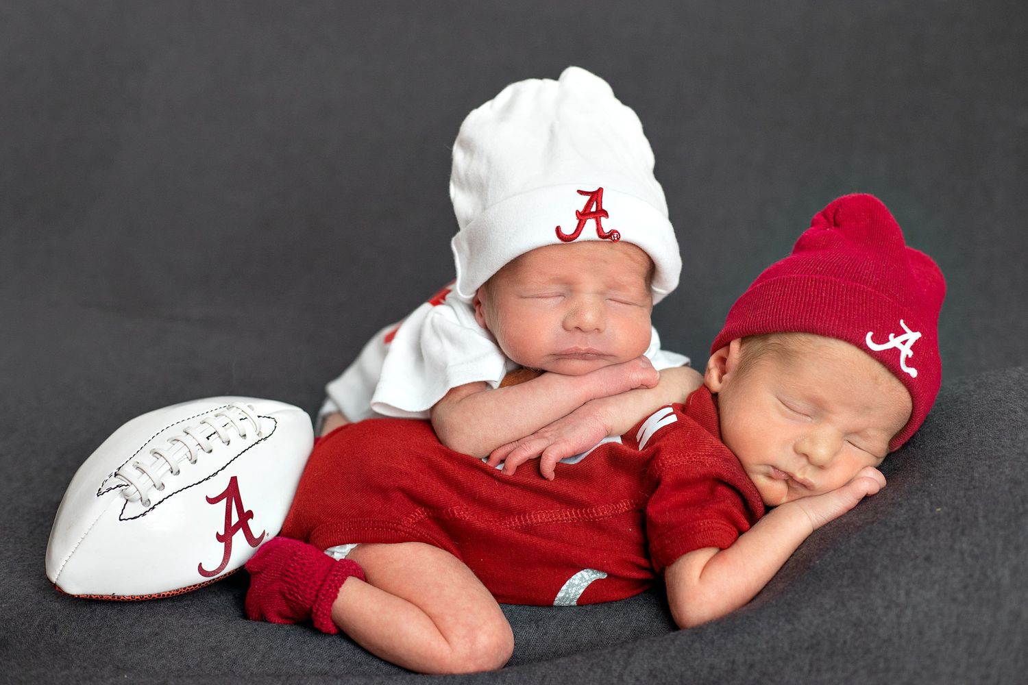 Two sleeping babies in crimson and white sports gear with football.