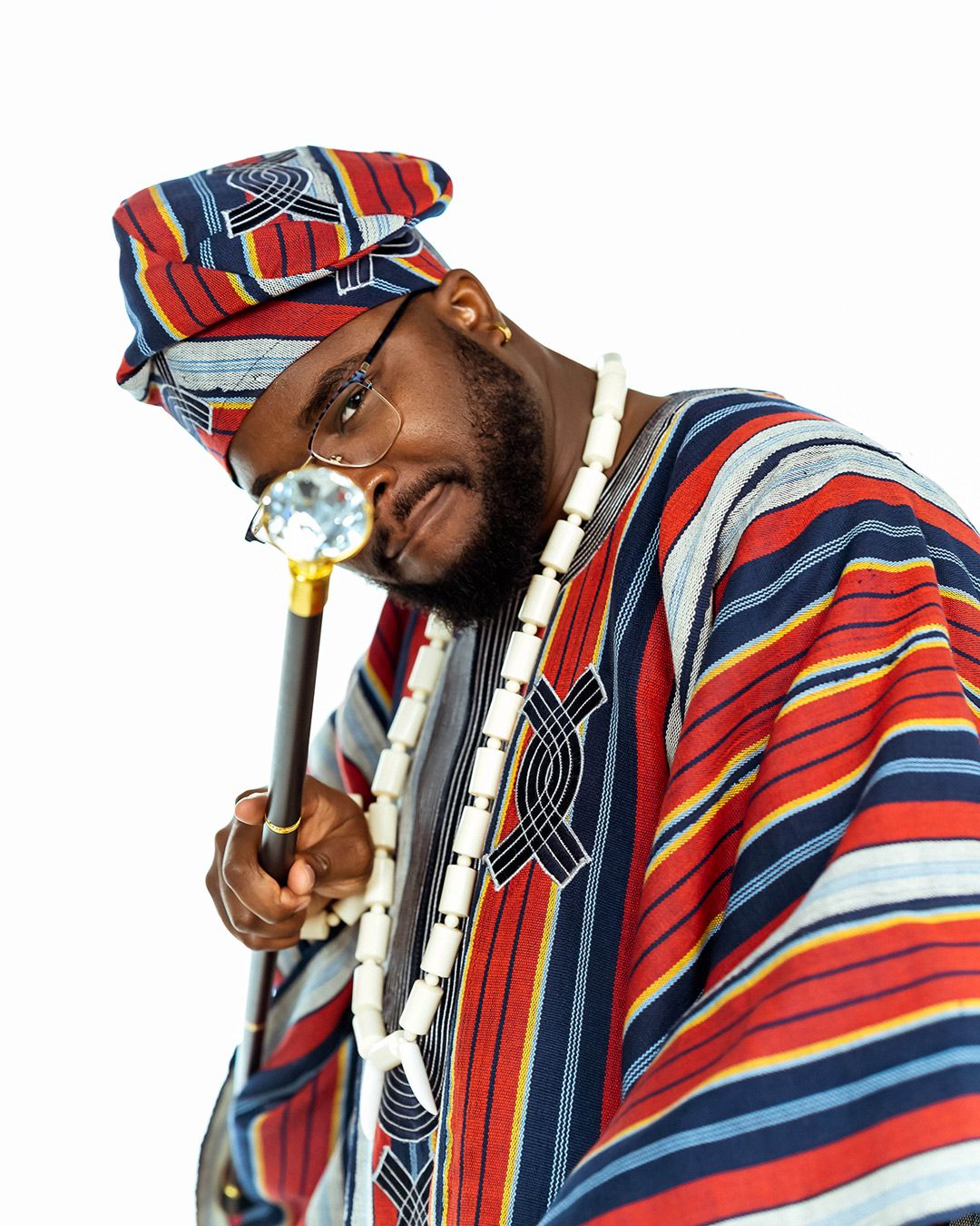 portrait of a young man wearing agbada, necklace and pointing a cane at the camera