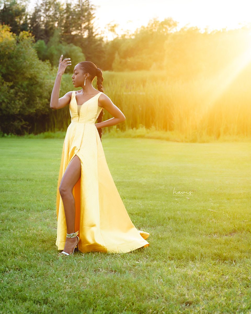 A young lady in yellow dress posing for a photograph on a field during sunset
