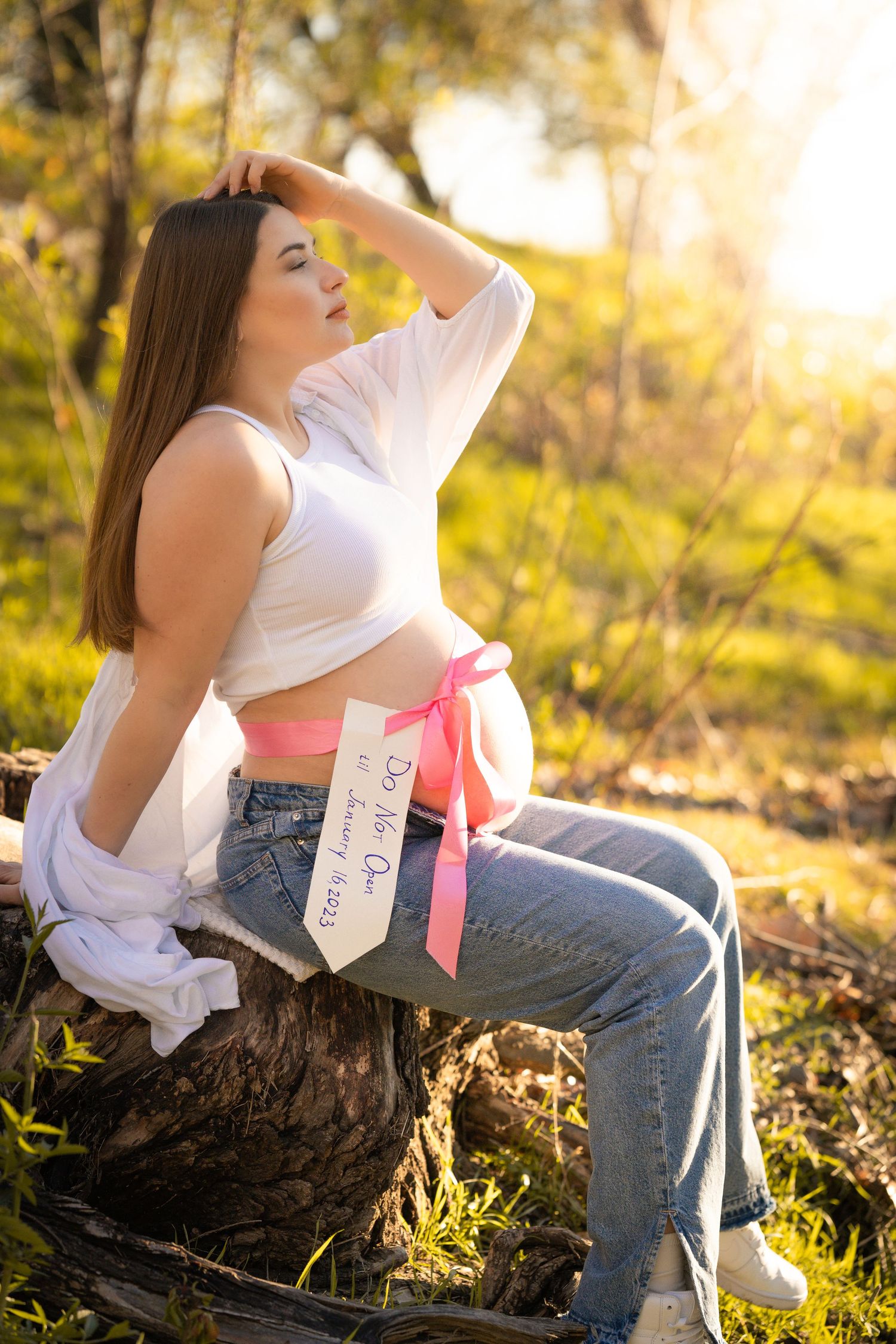 A breathtaking maternity photo in a sun-drenched field, her highlighted by soft, golden light,