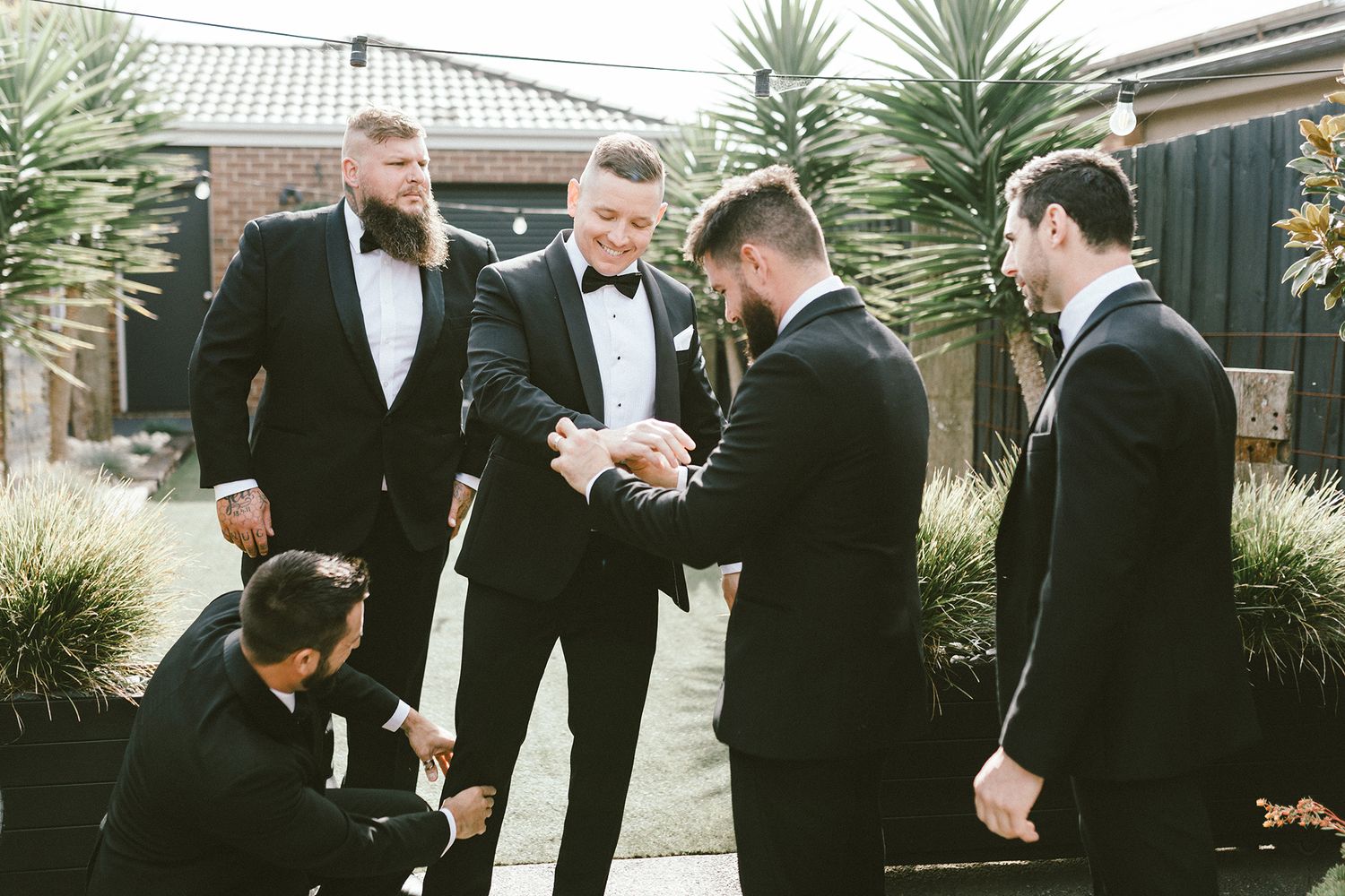 A wedding party shares a joyous moment while getting ready in their black tie attire.