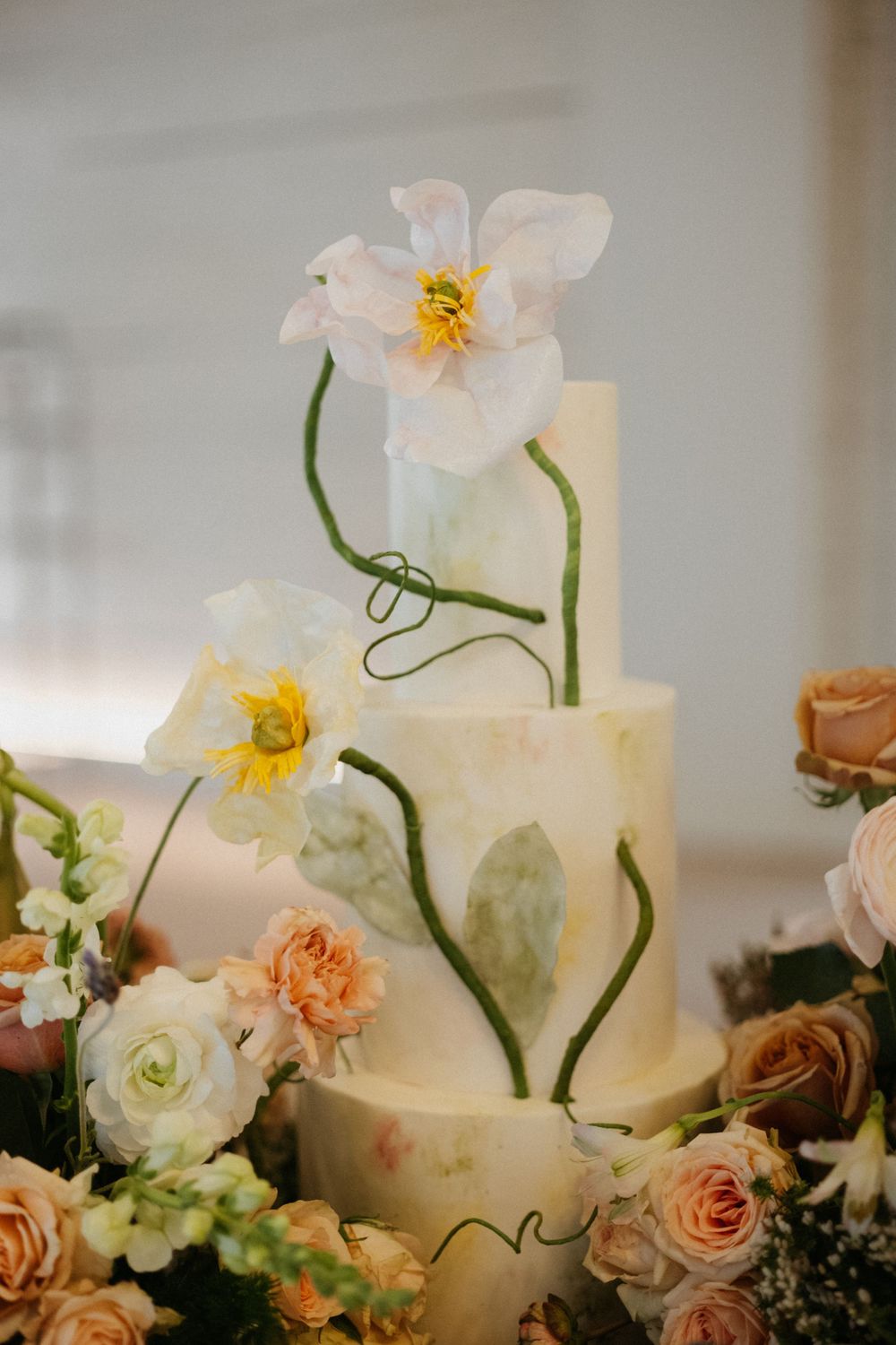 A delicate white wedding cake decorated with sugar flowers and fresh roses in peach and cream tones.