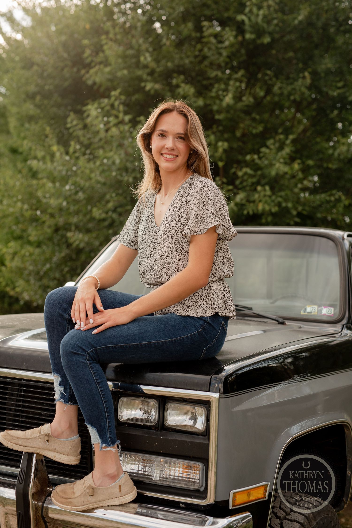 Casual outdoor portrait on the hood of a classic black truck with trees in background.