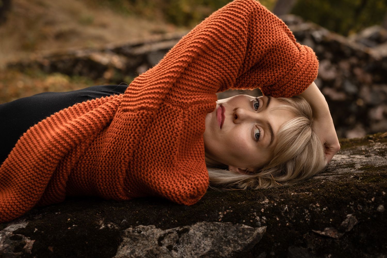 Portrait of a woman staring into camera from beneath her arm, while laying on her back.