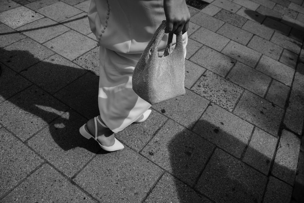 Close-up black and white photo of white shoes and handbag on stone pavement.