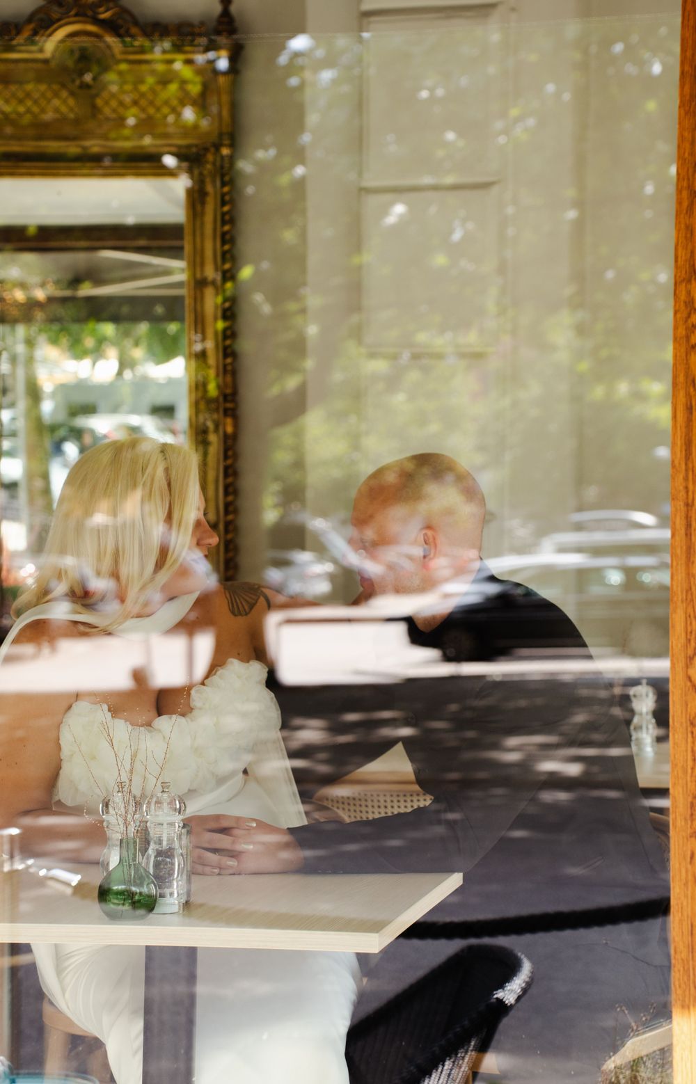 Artistic reflection through window of dining couple in sunlit cafe setting.