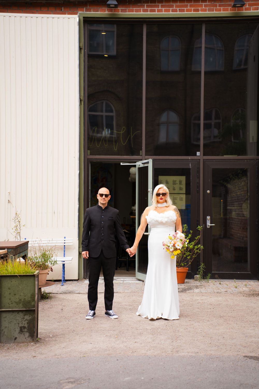Modern wedding couple poses outside industrial building with white walls.