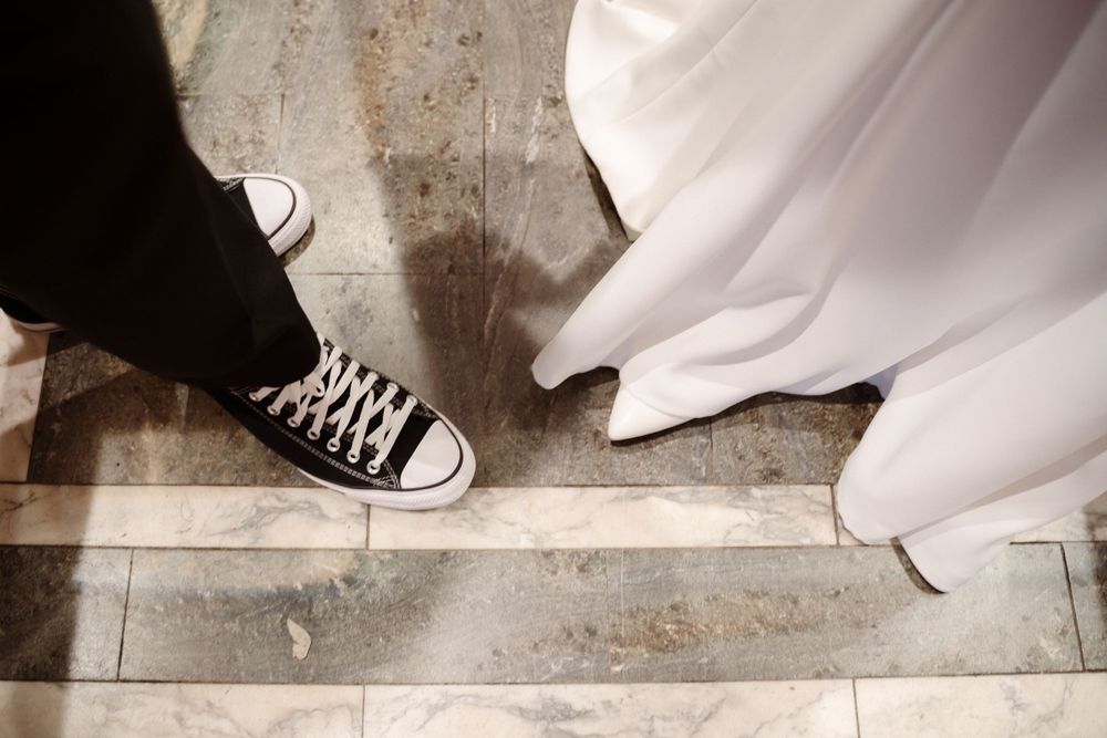 Artistic wedding photo showing contrast between white dress and black sneakers on floor.