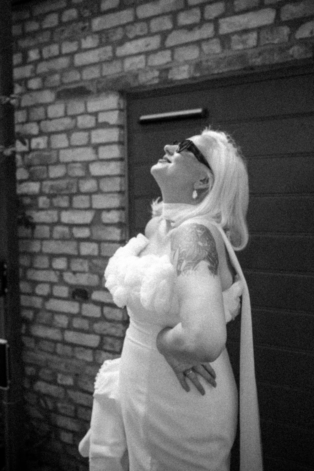 A black and white portrait of a bride laughing joyfully while wearing sunglasses.