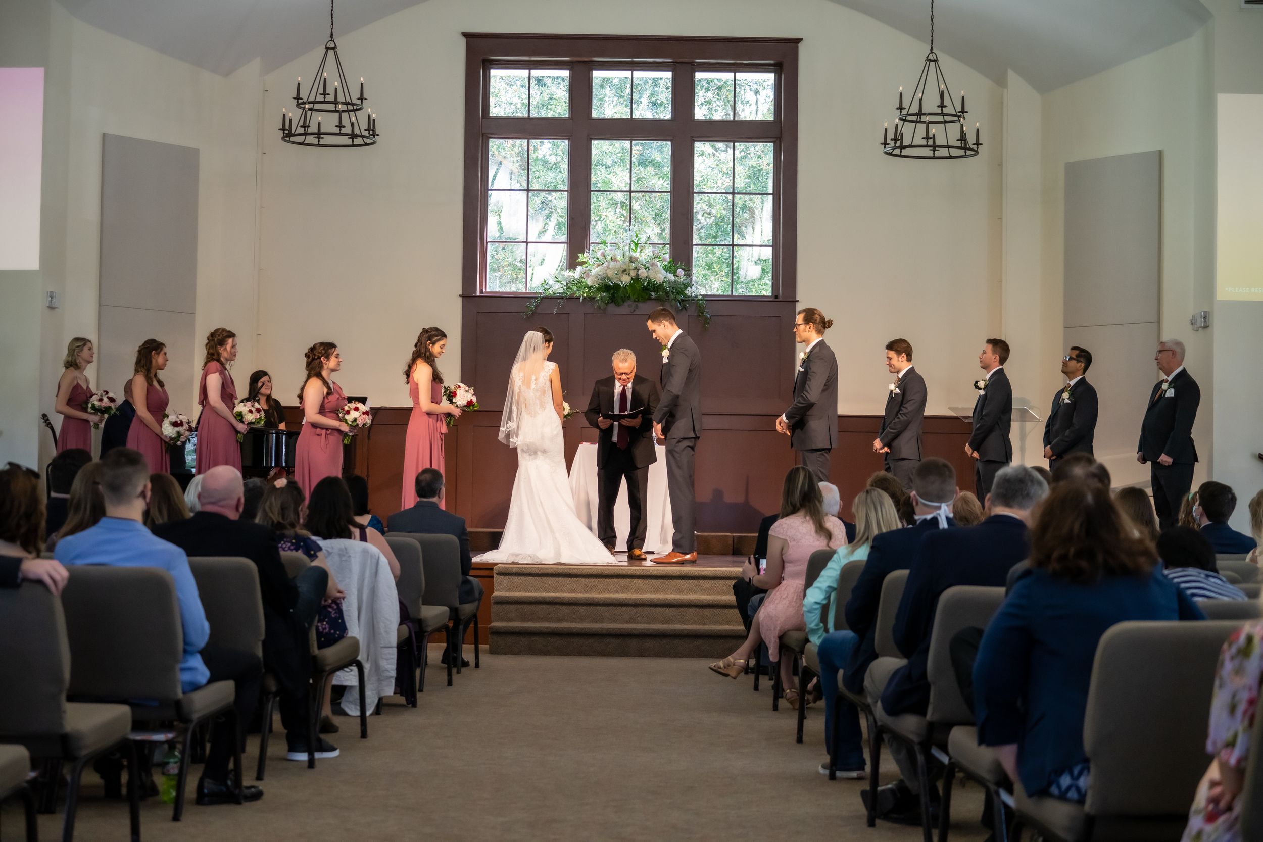 Wedding ceremony in progress inside chapel with guests seated in pews.