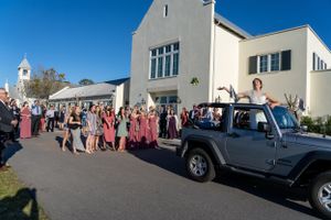 Wedding party and guests gather outside church with Jeep decorated for celebration.
