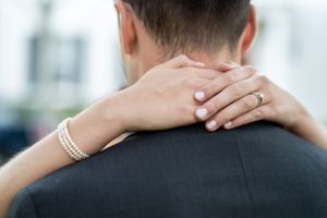Close-up of hands with pearl bracelet embracing neck during intimate moment.