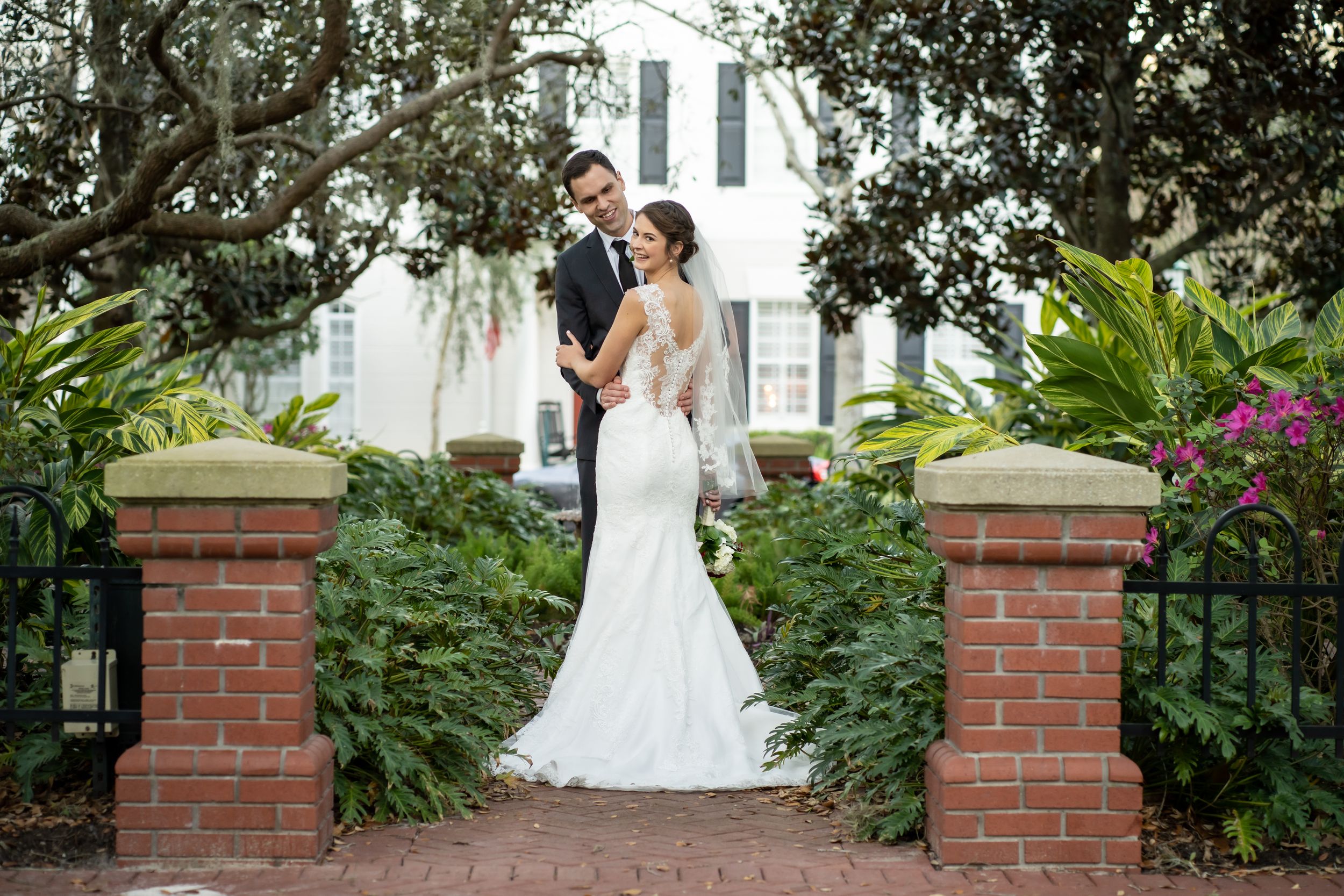 Elegant wedding photo between brick pillars with lush garden backdrop.