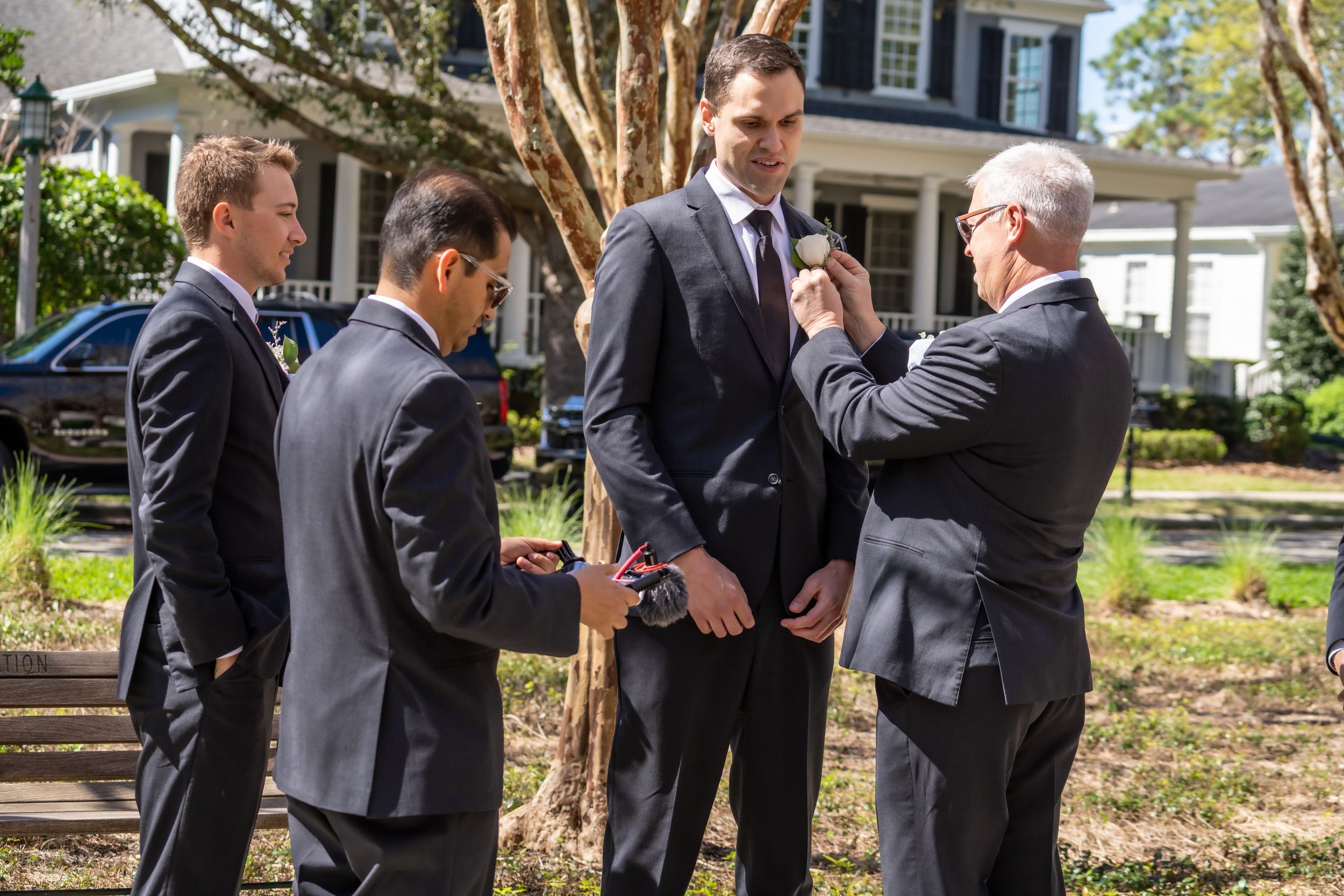 Groomsmen help adjust formal attire before wedding ceremony.