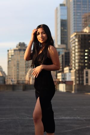 Cora Emilie Media Woman in black dress posing on rooftop with city skyline backdrop.