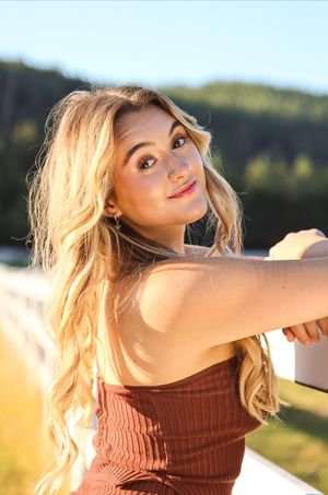 Cora Emilie Media Portrait in golden sunlight wearing rust-colored top against natural outdoor backdrop.