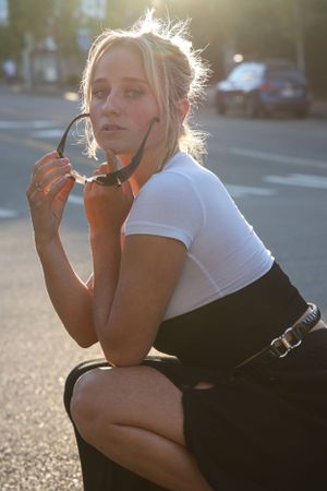 Cora Emilie Media A street style portrait in black and white outfit holding sunglasses at sunset.