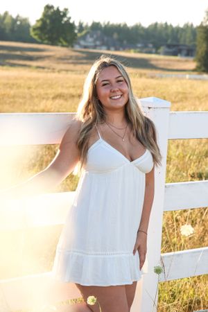 Cora Emilie Media A summer portrait in a white dress against a rustic white fence at sunset.