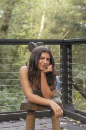 Cora Emilie Media Portrait on wooden deck overlooking forest with soft natural lighting.