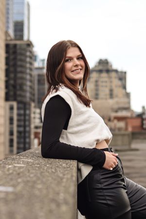 Cora Emilie Media Person in black and white layered outfit poses against urban cityscape backdrop.