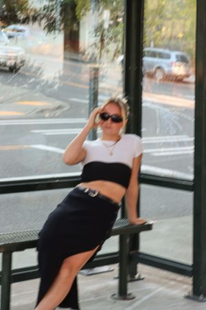 Cora Emilie Media A blurred motion portrait at a bus stop wearing sunglasses and casual attire.