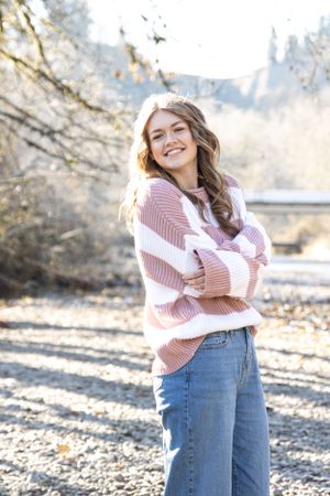 Cora Emilie Media Person in pink striped sweater and jeans poses outdoors in winter sunlight.