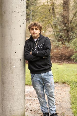 Cora Emilie Media A person in a black hoodie leans against a concrete pillar on a woodland path.