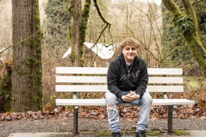 Cora Emilie Media Someone in casual wear sits alone on a white park bench surrounded by winter trees.