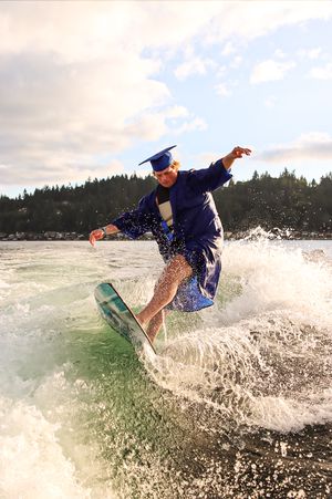 Cora Emilie Media Graduate performing trick on wakeboard while wearing graduation gown.