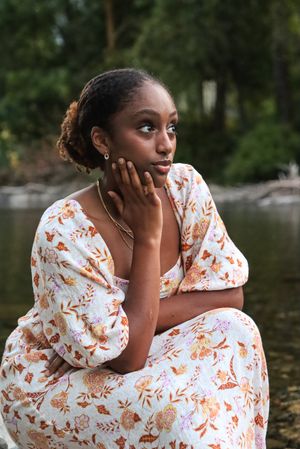 Cora Emilie Media A thoughtful portrait in a floral dress sitting by a serene lake.