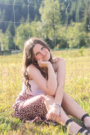 Cora Emilie Media Outdoor portrait in a field with wire fencing and mountains in background.