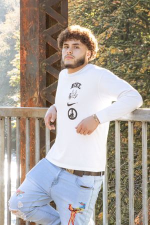 Cora Emilie Media Portrait at rustic bridge location wearing white long sleeve shirt and distressed jeans.