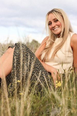 Cora Emilie Media Woman in floral dress sitting in field of wildflowers during golden hour.