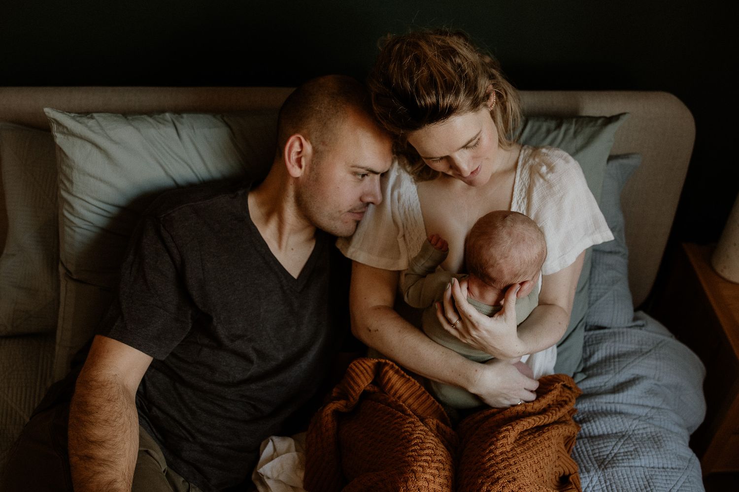 Intimate family moment captured on a bed with moody lighting and dark tones.