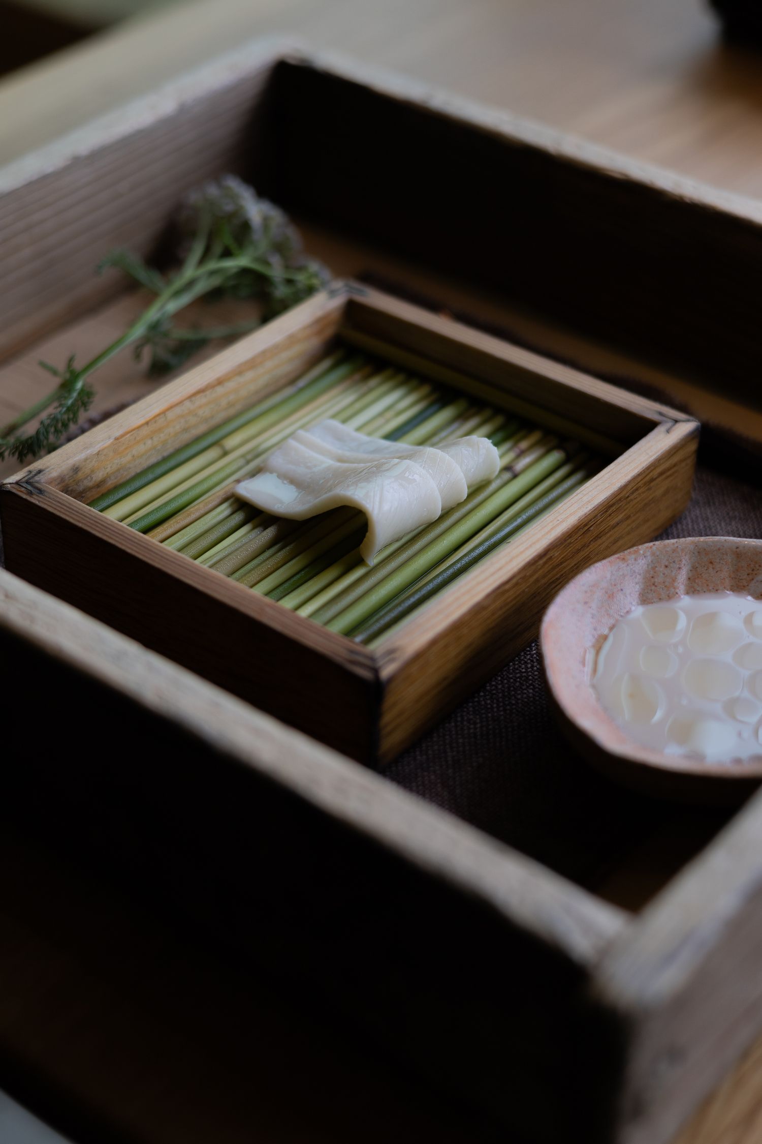 A wooden box contains fresh green bamboo stalks and white cloth napkins.