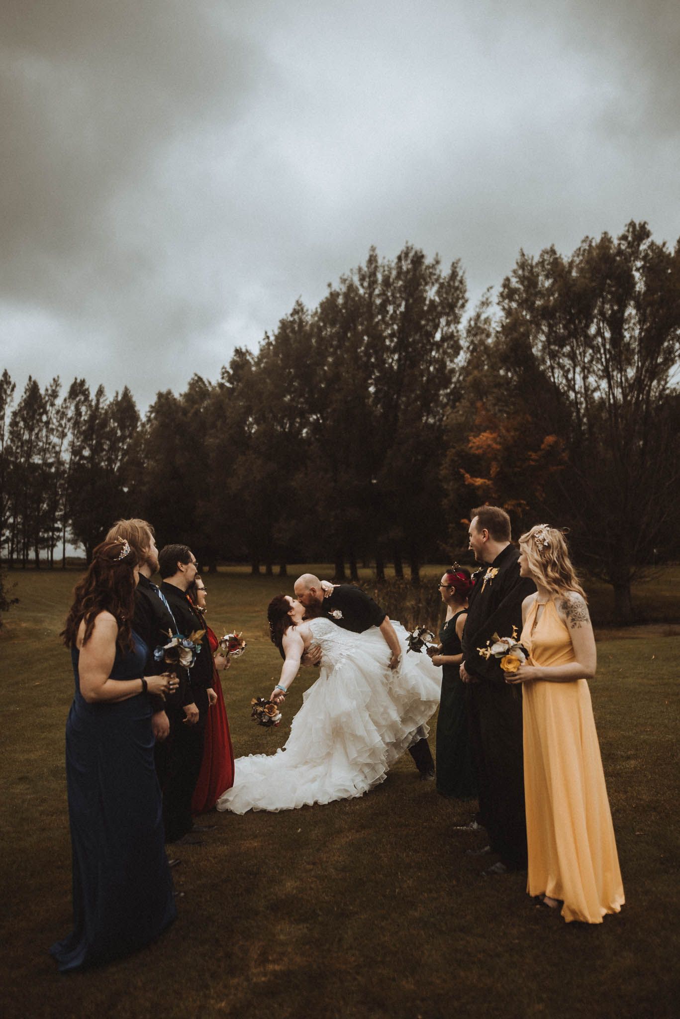A wedding party gathers on a moody fall day with bridesmaids in dark dresses.