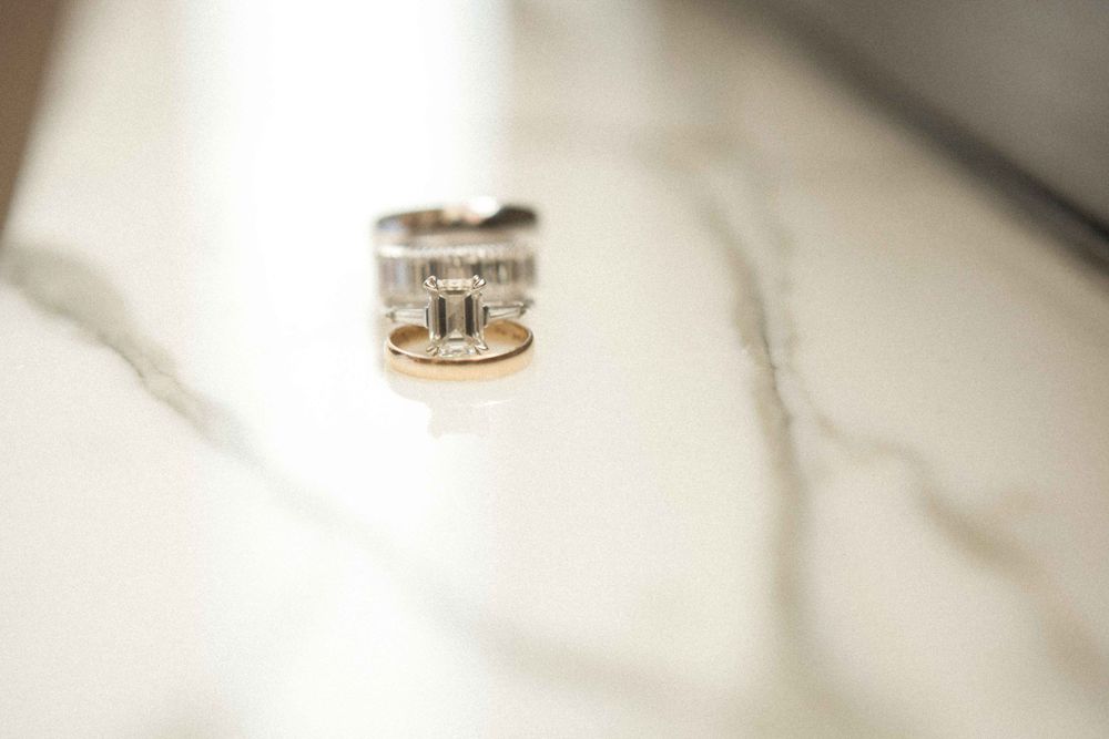 A silver and gold two-tone ring with intricate design details sits on a white textured surface in soft focus.