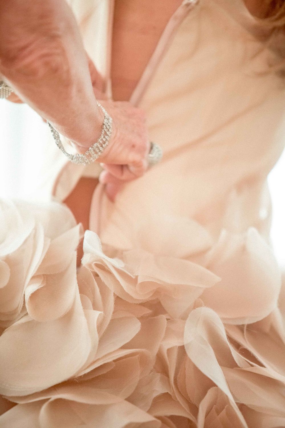 Close-up of delicate ruffled layers on a blush wedding gown with sparkly bracelet detail.