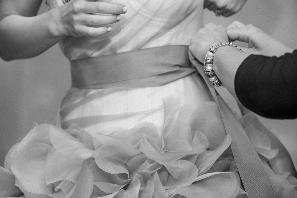 Close-up black and white image of someone adjusting delicate ruffles on an elegant white wedding dress.