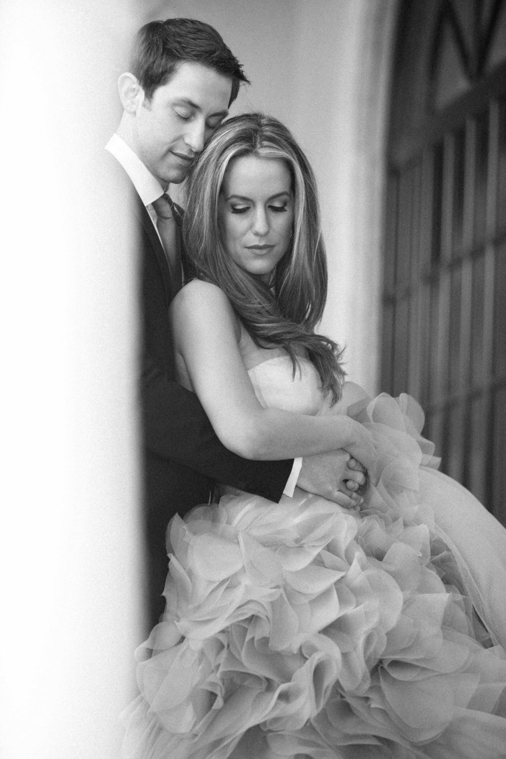 A romantic black and white wedding portrait shows embracing couple with bride wearing a flowing ruffled gown.