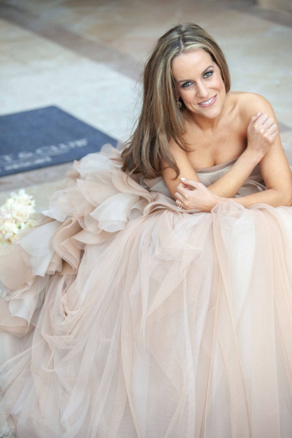 A person wearing a delicate blush tulle gown lies on the floor with white flowers nearby.