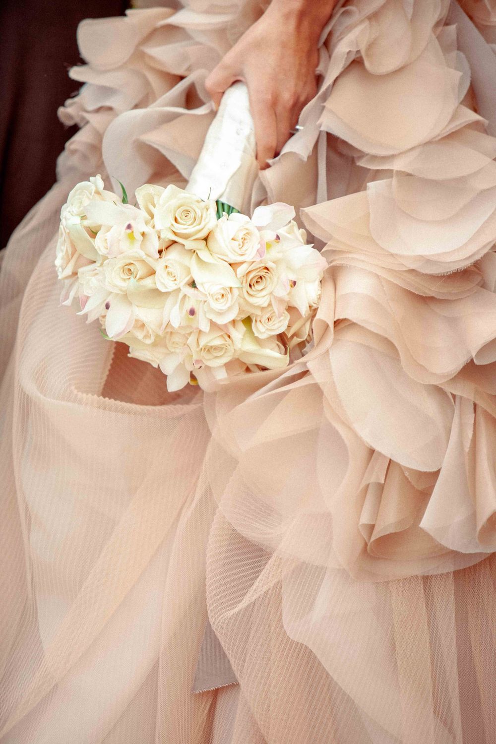 Close-up detail of blush pink ruffled tulle fabric from a wedding dress with white rose bouquet accent.