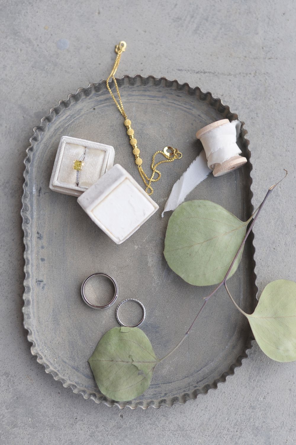 Wedding accessories on grey tray including rings, jewelry, and eucalyptus leaves.